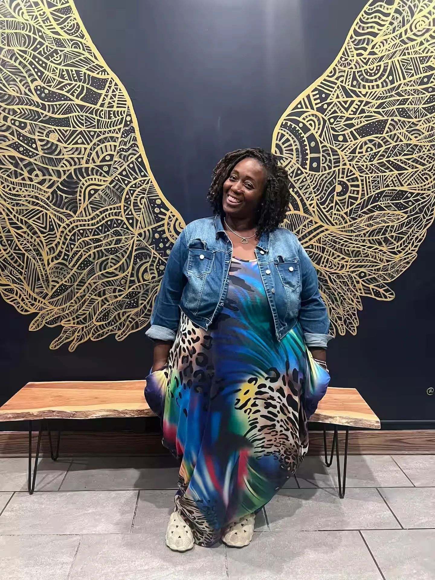 Tieshia Henry seated in front of a mural of golden wings